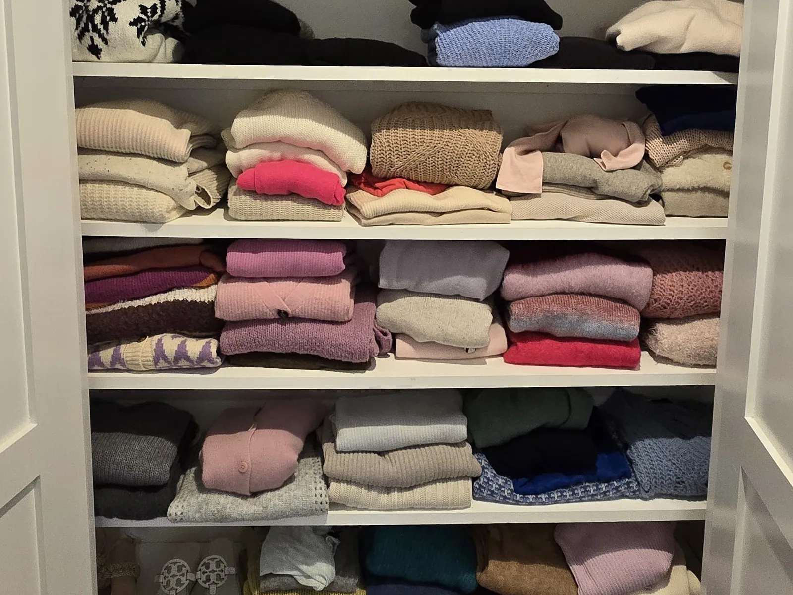 Linen closet with folded towels and sweaters stacked by shelf
